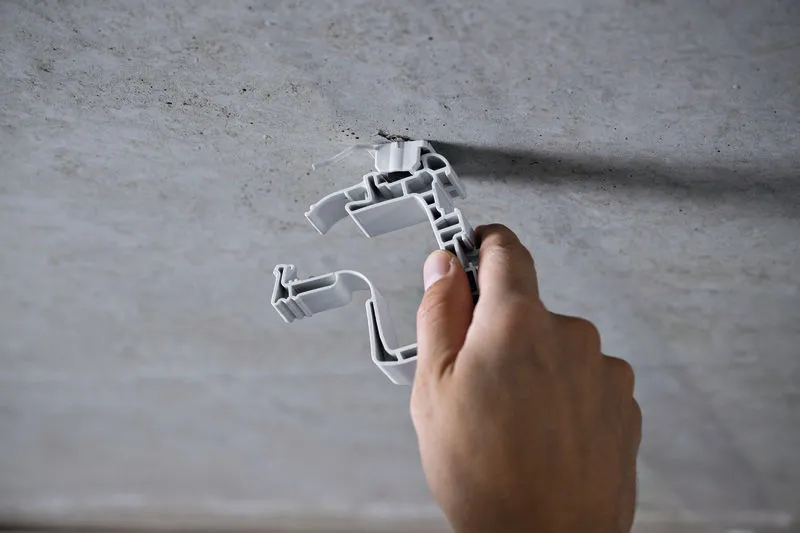 A person attaches a plastic clip to a concrete ceiling.