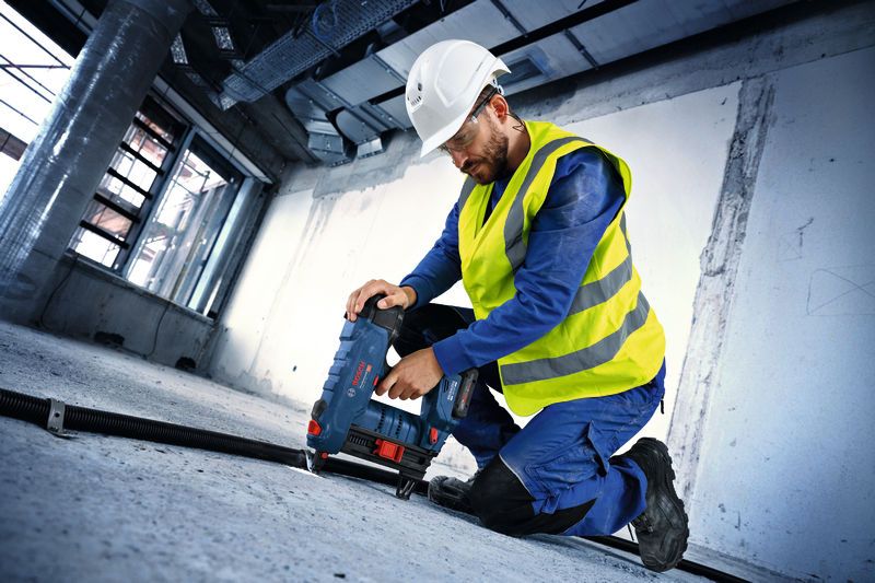 A worker wearing safety equipment fastens conduit to a concrete floor with a cordless concrete nailer.