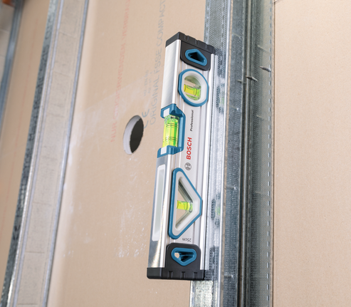 Spirit level aligned against a drywall panel with a cutout.