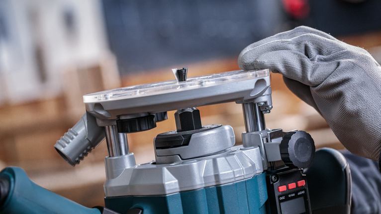 Person wearing safety equipment adjusts a power router in a workshop.
