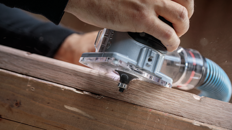 Person uses a handheld router to shape the edge of a wooden board.