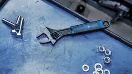 Adjustable wrench lying on a workbench next to bolts, nuts, and washers.