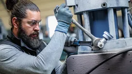 Person wearing safety equipment tightens a large metal bolt with two wrenches.