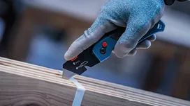 Person wearing safety equipment cuts packing strap with utility knife.
