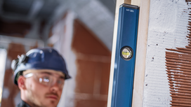 Person wearing safety equipment checks wall alignment with a spirit level.