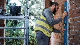 Person wearing safety equipment checks brick wall alignment with a spirit level.
