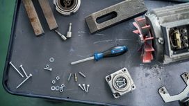 Screwdriver and assorted bolts, nuts, and machine parts laid out on a metal workbench.