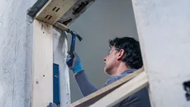 A person wearing safety equipment hammers a nail into a wooden frame.