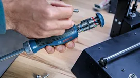 Person selects a screwdriver bit from a multi-bit hand tool beside machinery.