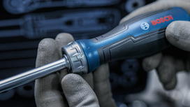 Person wearing safety equipment holds a blue and black screwdriver.