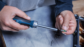 Person holding a screwdriver and selecting a screwdriver bit at a workbench.