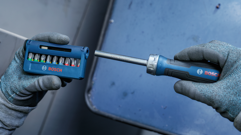 Person wearing safety equipment selects a screwdriver bit from a set.
