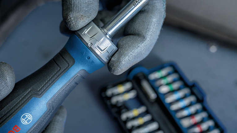 Person wearing safety equipment holds a ratchet handle near a socket set.