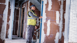 Person wearing safety equipment checks wall alignment with a digital level.