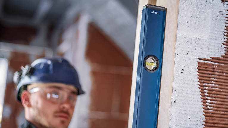 Person wearing safety equipment checks a vertical level on a wooden beam.