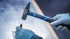 Person wearing safety equipment uses a hammer and punch on a metal plate.