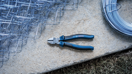 Wire cutter with blue handles lying on a stone slab next to metal fencing and rolled wire.