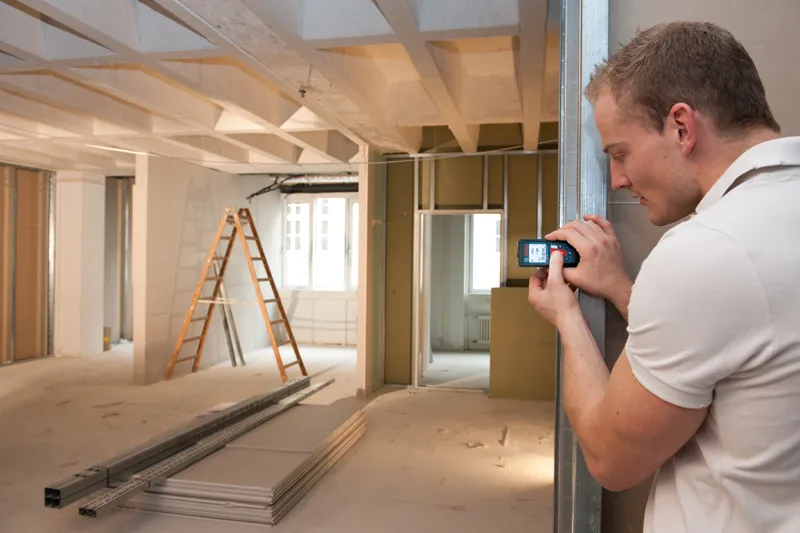 Person measuring a room with a laser measure in a building under construction.