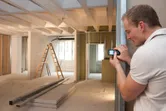 Person measuring a room with a laser measure in a building under construction.