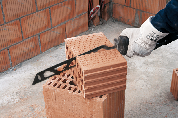 Людина в захисному спорядженні розрізає порожнисту цеглу за допомогою електропилки.