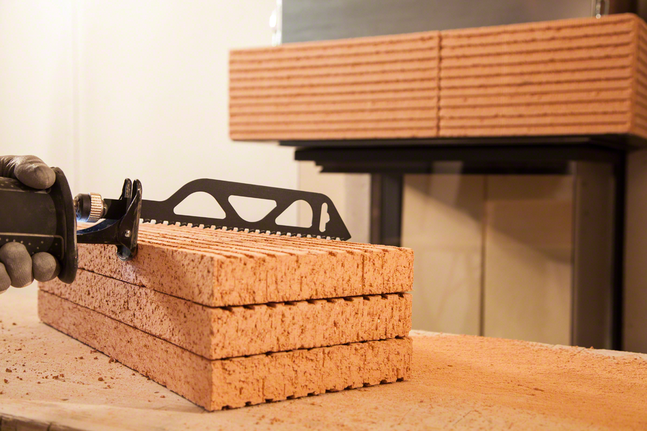 Людина в захисному спорядженні ріже складені цеглини зворотно-поступальною пилкою.