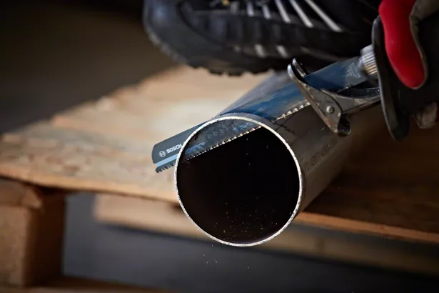 Працівник у захисному спорядженні використовує зворотно-поступальну пилку для різання металевої труби.