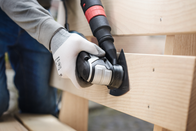 Працівник у захисному спорядженні шліфує дерев'яні дошки за допомогою багатофункціонального інструменту.