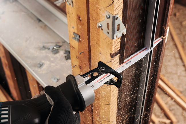 Працівник у захисному спорядженні використовує зворотно-поступальну пилку для розрізання дерев'яної балки.