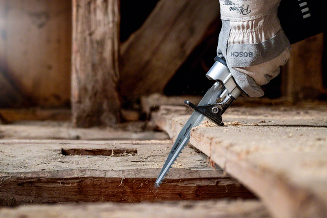 Працівник у захисному спорядженні розпилює дерев'яну підлогу сабельною пилкою.