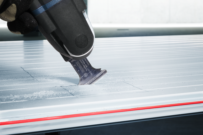 Людина в захисному спорядженні використовує багатофункціональний інструмент для вирізання прямих ліній у металевому листі.