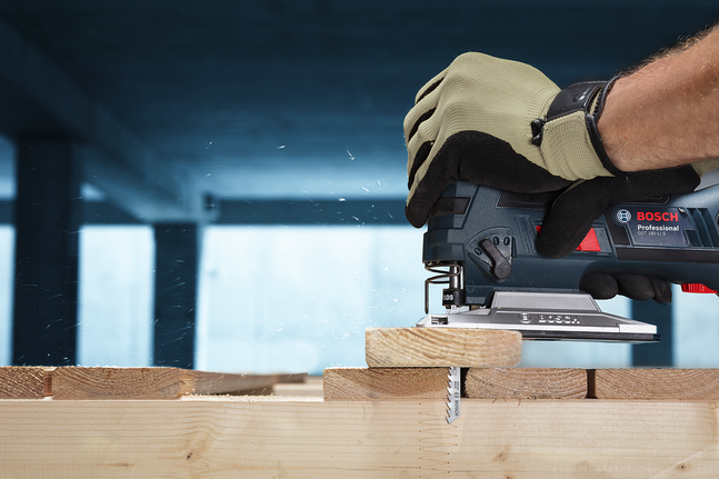 Людина в захисному спорядженні розрізає дерев'яні дошки лобзиком.