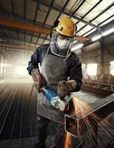 Людина в захисному спорядженні шліфує метал, утворюючи яскраві іскри на заводі.