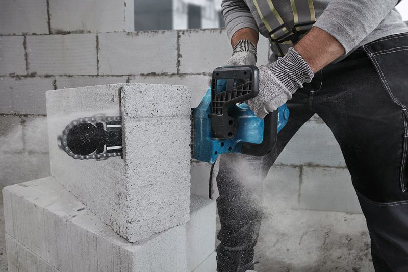 Людина в захисному спорядженні ріже газобетонний блок за допомогою бензоріза.