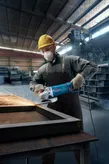 Людина в захисному спорядженні шліфує металевий каркас кутовою шліфувальною машинкою в майстерні.