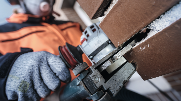 Людина в захисному спорядженні ріже коричневу плитку електроінструментом.