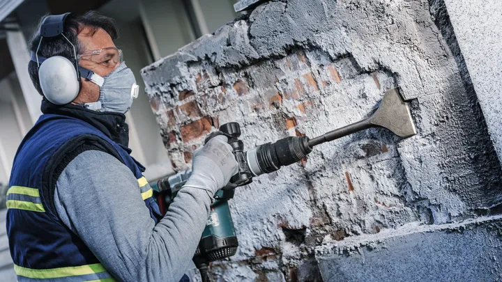 Працівник у захисному спорядженні зрубує бетон зі стіни за допомогою перфоратора.
