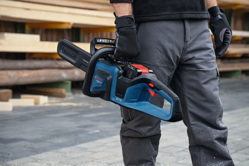 Людина в захисному спорядженні тримає акумуляторну бензопилу на складі пиломатеріалів.