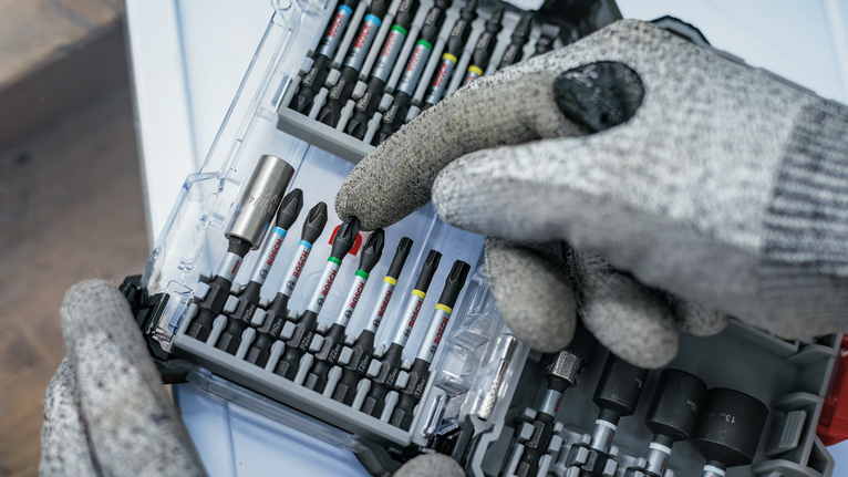 Людина в захисному спорядженні вибирає викрутку з організованого набору інструментів.