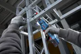 Людина в захисному спорядженні використовує бездротовий кутовий дриль на металевому каркасі.