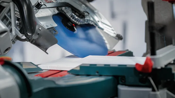 Дискова пилка ріже білу дошку на стенді для торцювальної пилки.