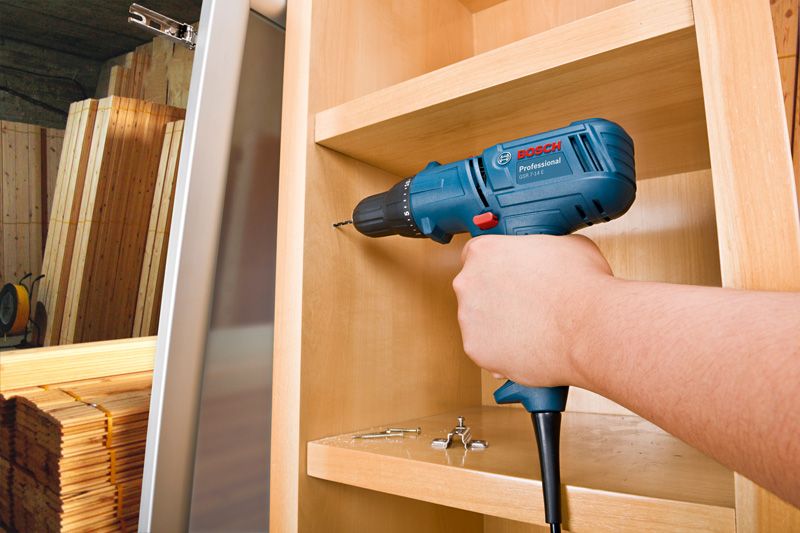 Una persona perfora un agujero en un armario de madera utilizando un taladro.