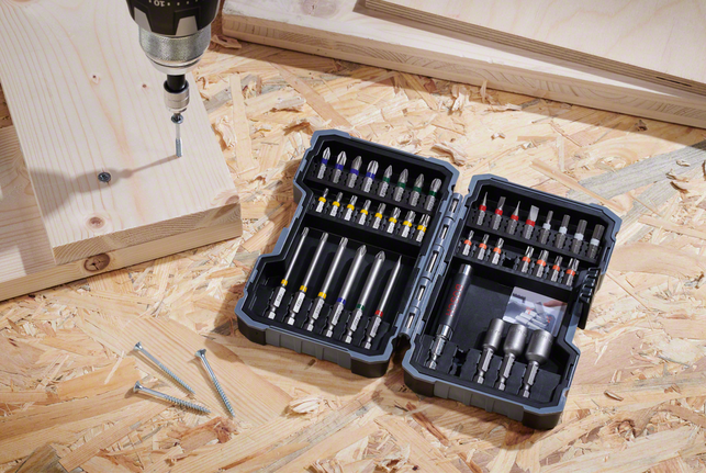 Taladro atornillador colocado sobre una superficie de madera contrachapada junto a tornillos y tablones de madera.