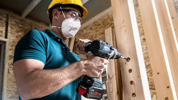 Persona que usa equipo de seguridad perfora agujeros en vigas de madera.