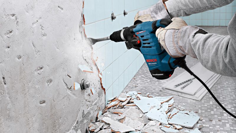 Una persona que usa equipo de seguridad utiliza un martillo rotatorio para quitar azulejos de una pared.
