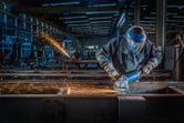 Una persona que usa equipo de seguridad muele metal con una amoladora angular, produciendo chispas.