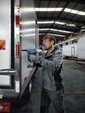 Un trabajador que usa equipo de seguridad usa un taladro inalámbrico para fijar metal a un remolque.