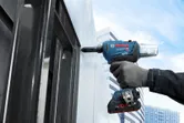 Una persona que usa equipo de seguridad utiliza una llave de impacto inalámbrica en un marco de acero.