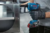 Una persona que usa equipo de seguridad utiliza una pistola remachadora inalámbrica sobre un marco de metal.