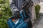 Una persona con equipo de seguridad inserta una batería en un soplador de hojas inalámbrico al aire libre.