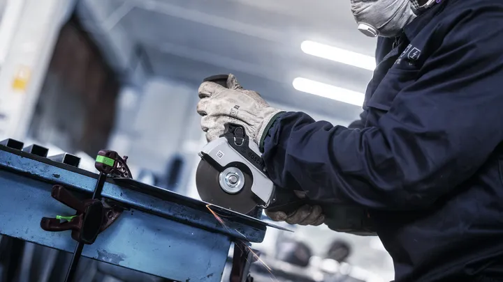 Una persona que usa equipo de seguridad muele metal con una amoladora angular, produciendo chispas.